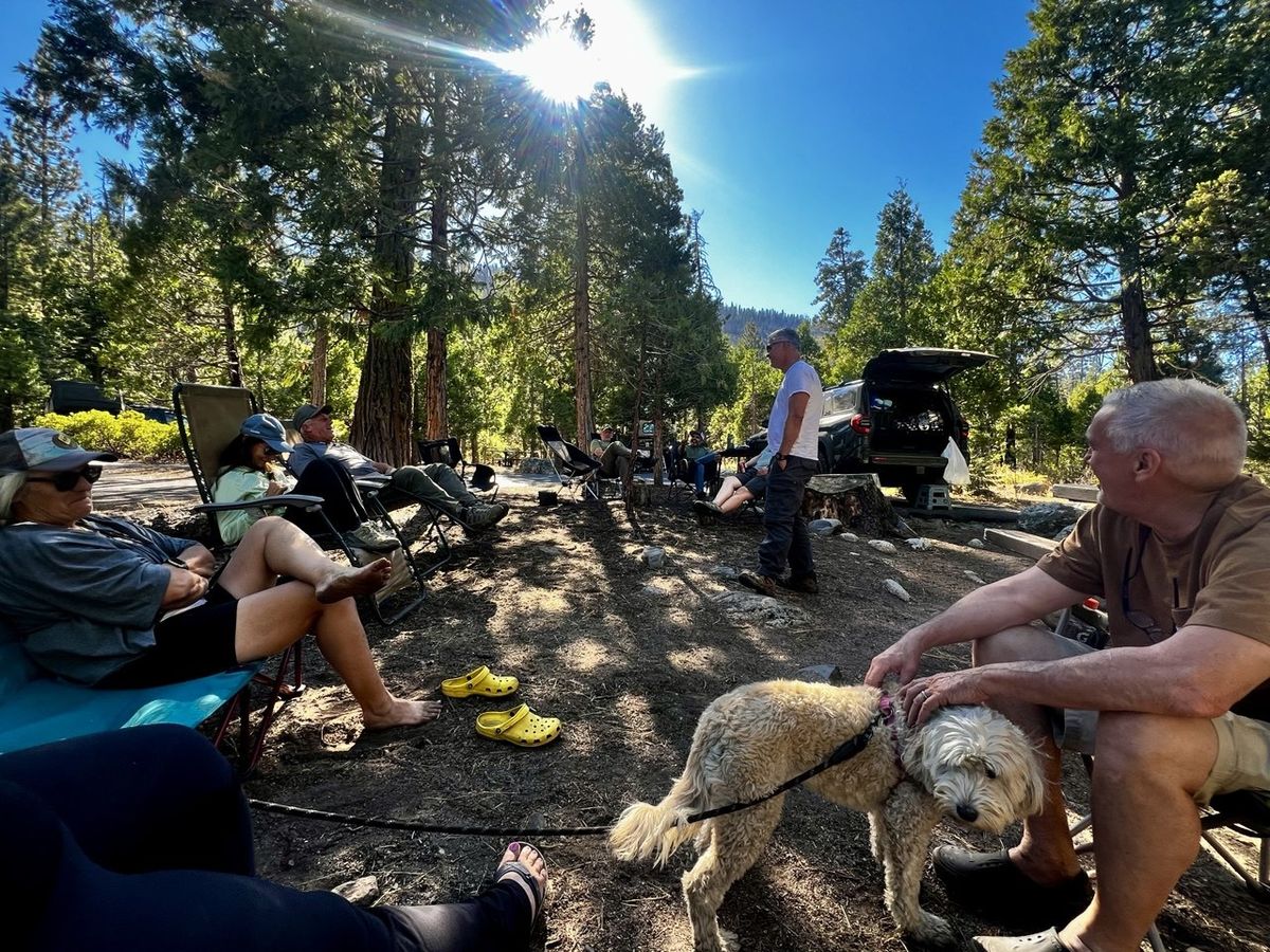 The group relaxing around camp with black SUV and petting the camp dog