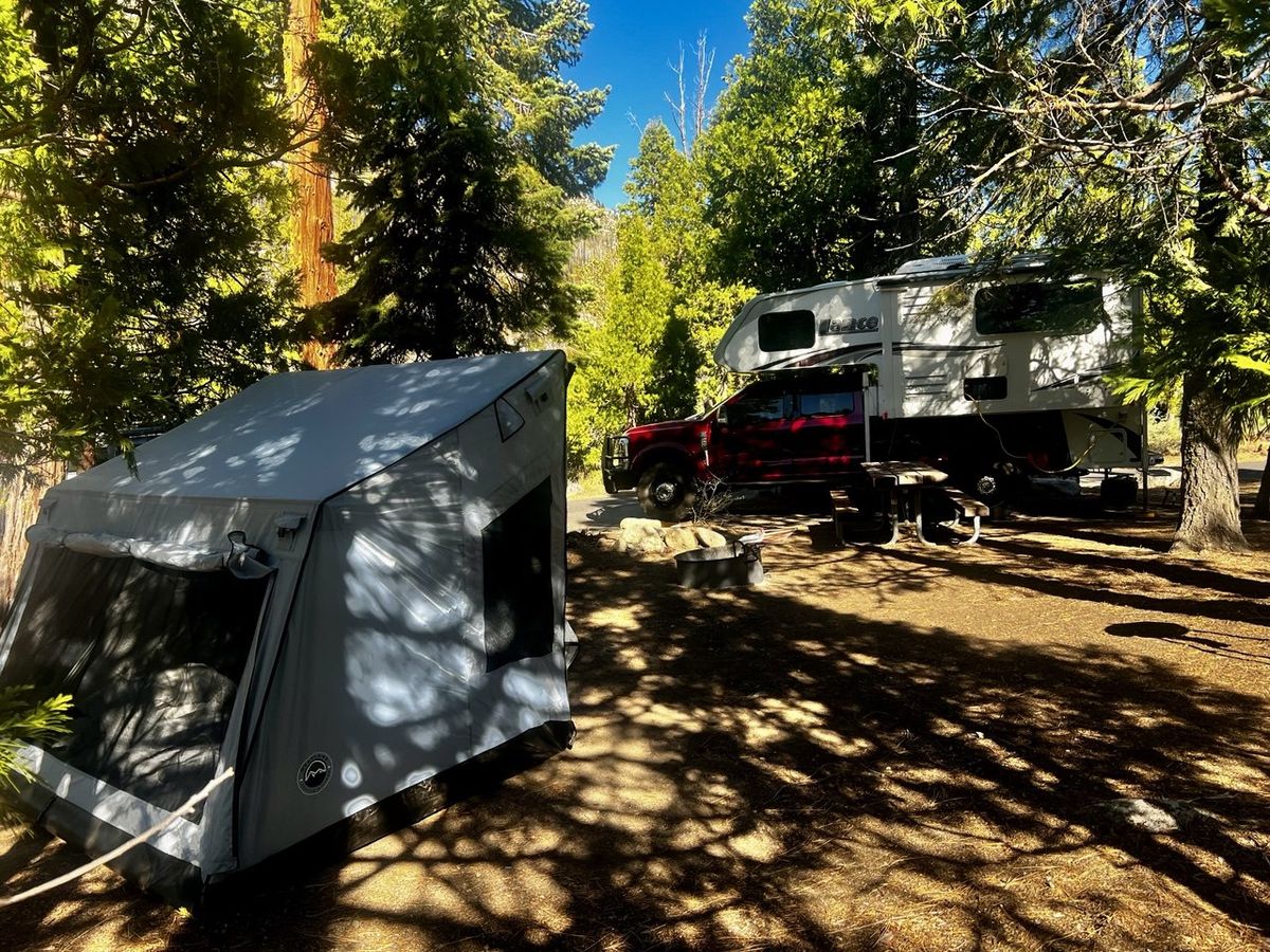 Campsite with gray tent and red truck with LANCE slide-in camper