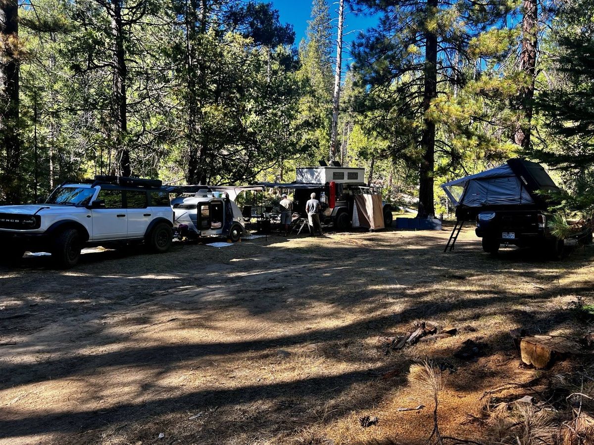 Overland basecamp with white Ford Bronco, teardrop camper, and truck campers