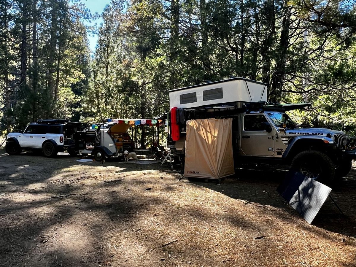 Tan Jeep Rubicon with KICKASS side tent alongside white SUV and teardrop camper