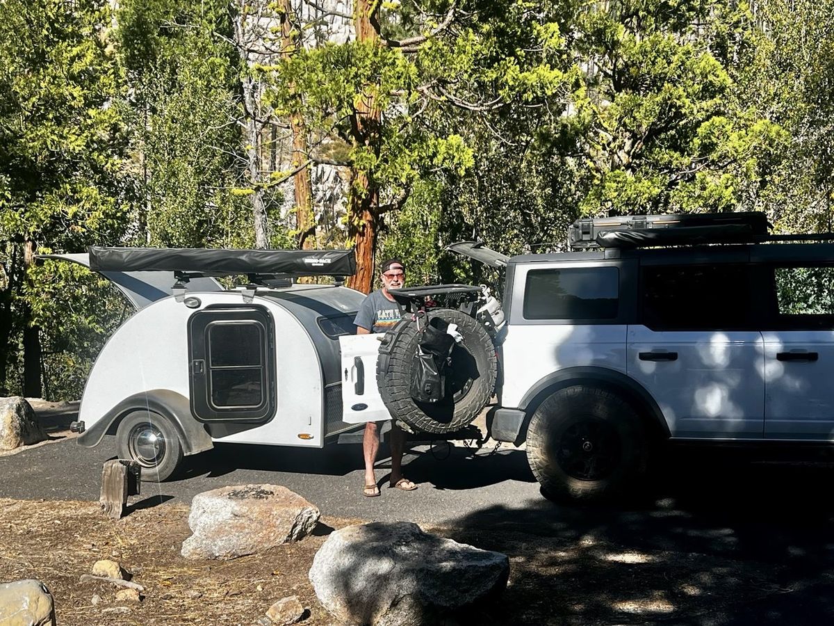 White off-road SUV and teardrop camper trailer with rear hatches open at camp