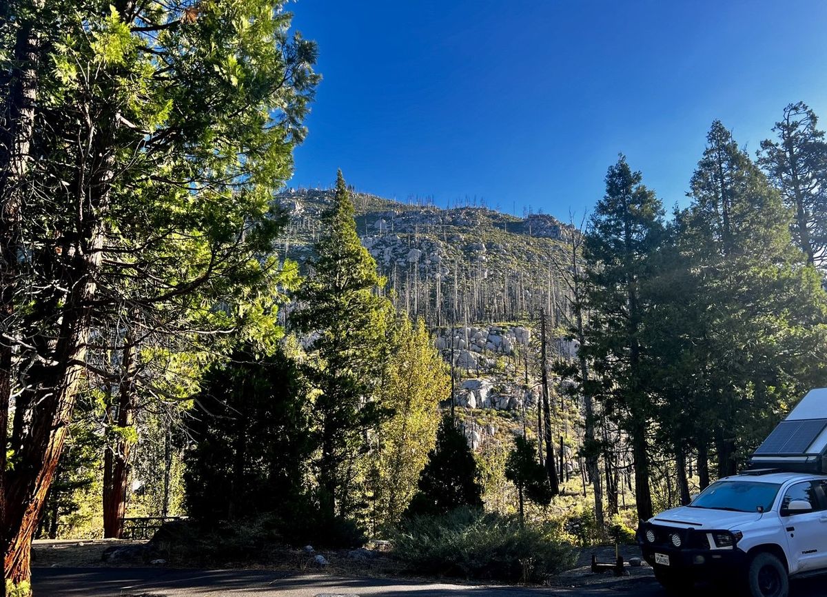 White Toyota with rooftop tent parked on a turnout overlooking the post-fire hillside
