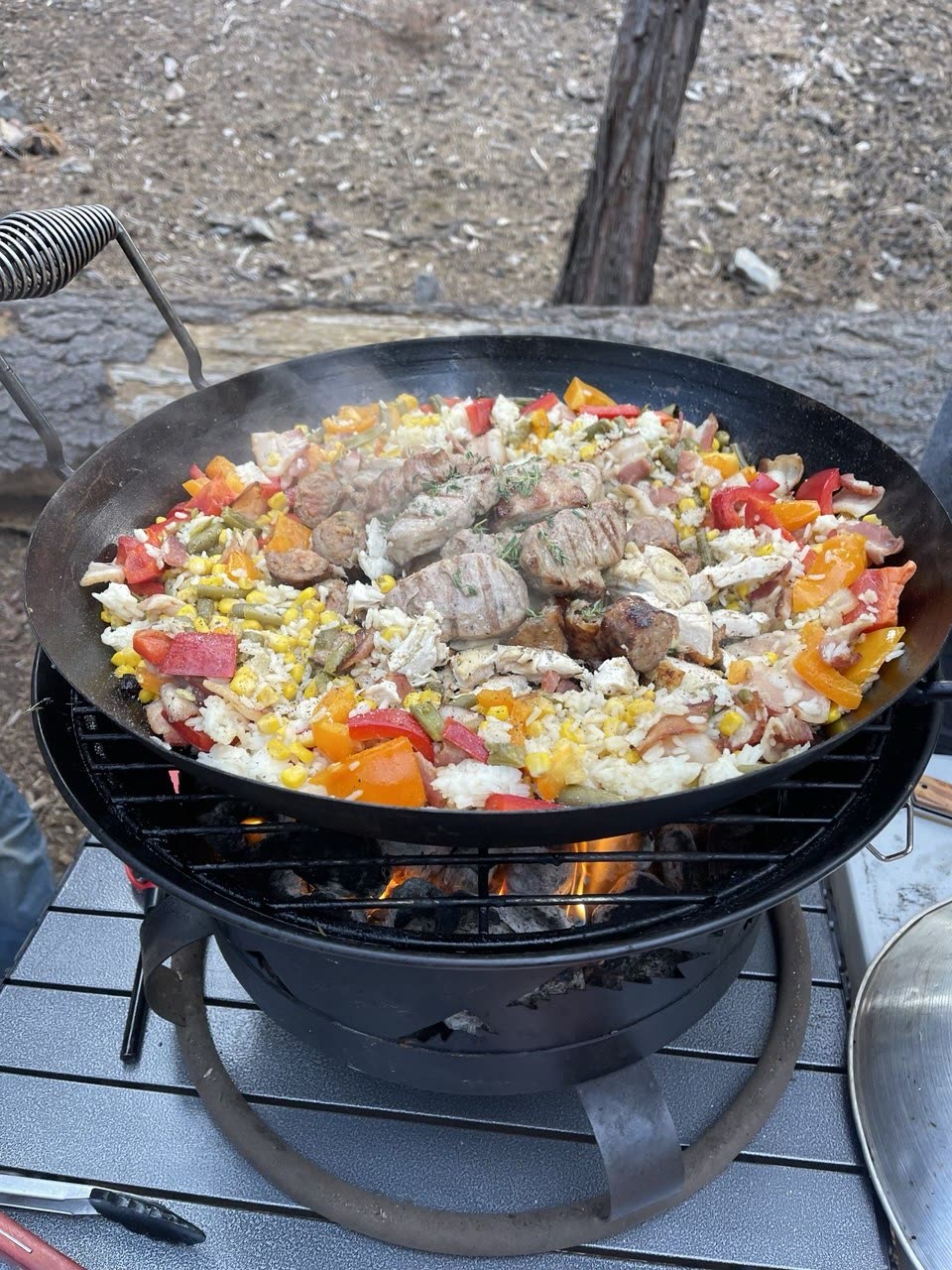 A paella pan of rice with grilled meat, sausage, peppers and green beans cooking over a portable stove at a Tahoe National Forest campsite.