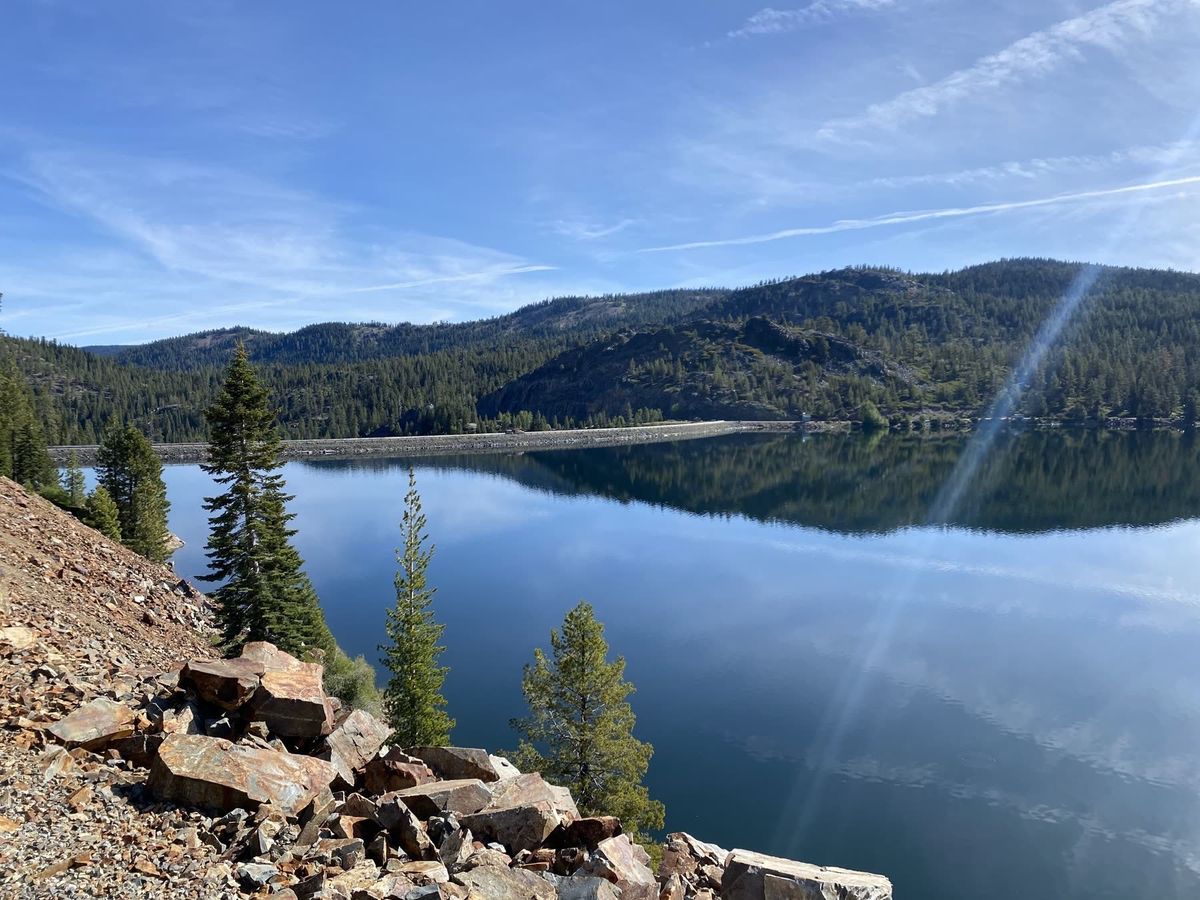 Scenic alpine vista of Bowman Lake with calm water reflecting pine-covered ridges and the Bowman Lake dam structure in Tahoe National Forest